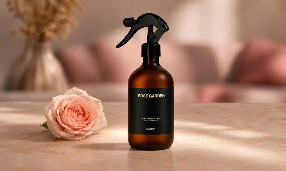 An amber glass spray bottle with a black trigger mechanism and label sits centered on a light stone surface, with gold text reading 'ROSE GARDEN HOME FRAGRANCE MIST PARFUM D'AMBIANCE LANSY'.