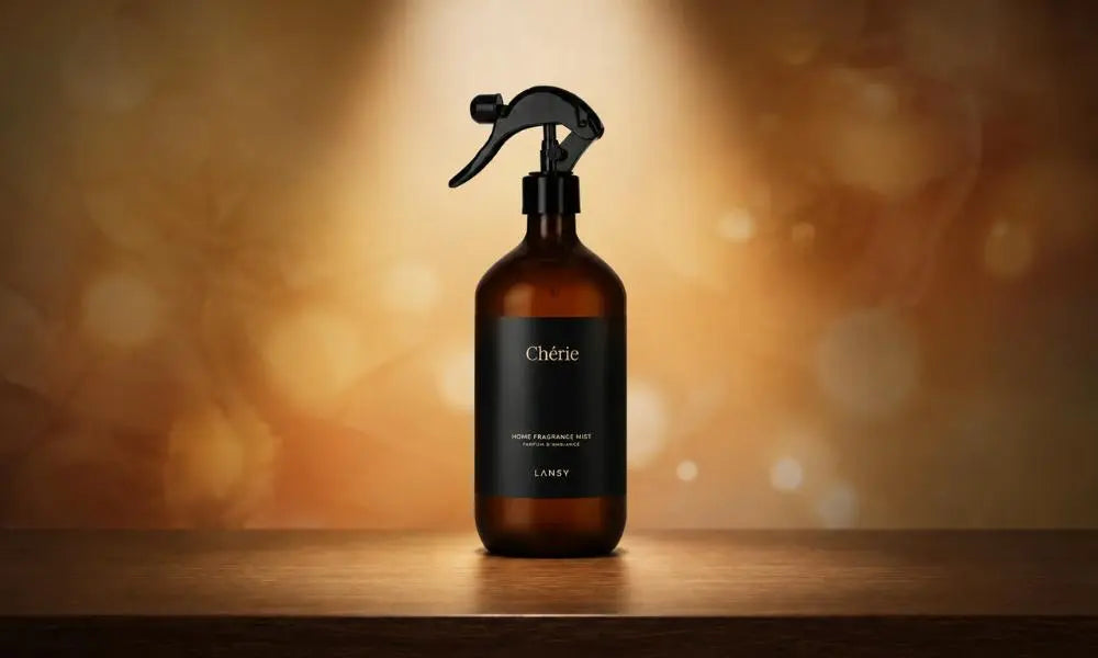 An amber spray bottle labeled "Chérie" is centered on a wooden surface, set against a warm, blurred bokeh background with soft lighting.