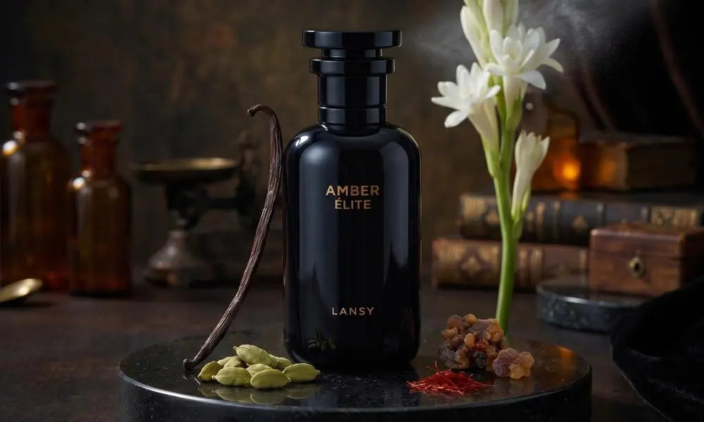 A sleek, glossy black perfume bottle labeled "AMBER ÉLITE by LANSY" surrounded by raw ingredients like vanilla beans, cardamom pods, and white flowers on a dark, rustic background.