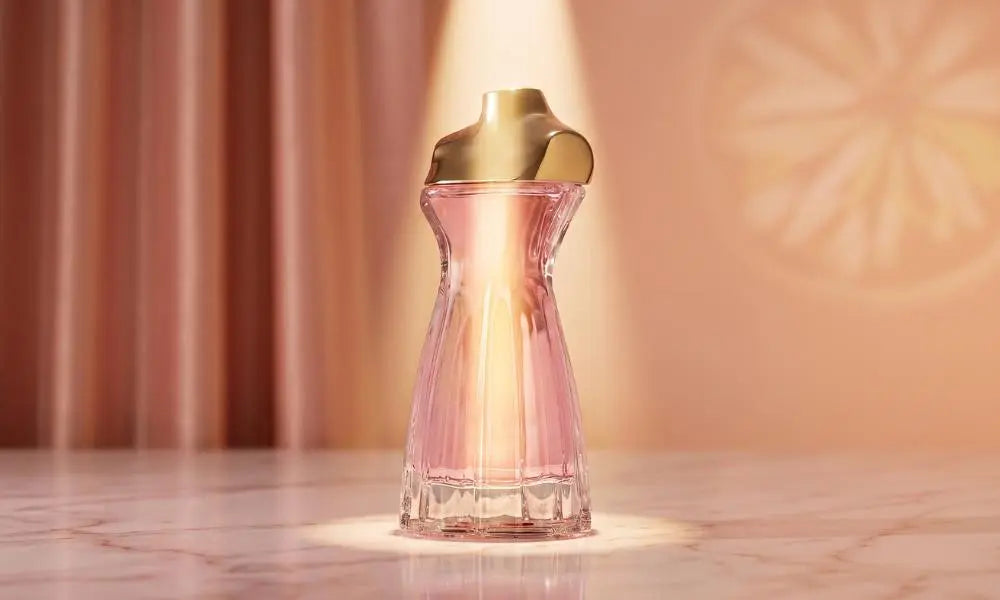 Dress-shaped perfume bottle with pink liquid and gold cap on marble.