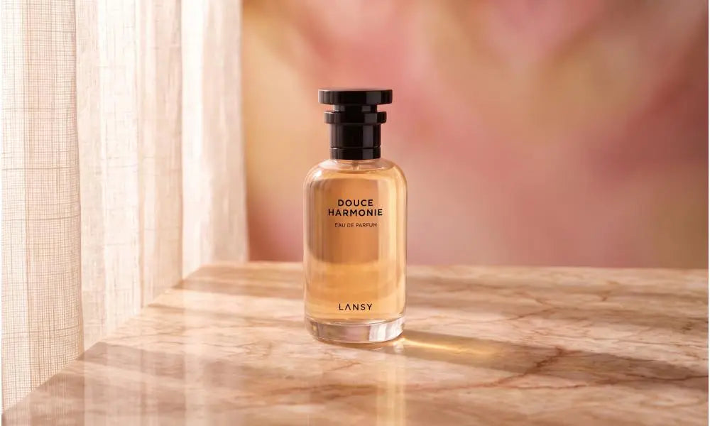 "A bottle of Lansy 'Douce Harmonie' perfume on a marble table with a soft-focus, warm pink background."