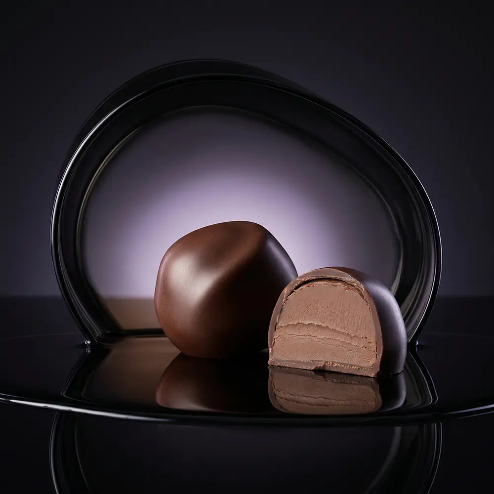 Chocolate truffles with layered filling on a glossy black reflective surface.