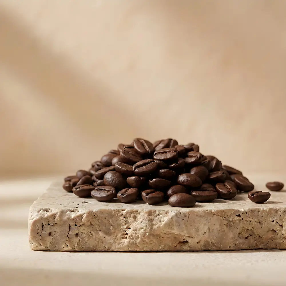 Roasted coffee beans on a rough stone slab against a warm beige background.