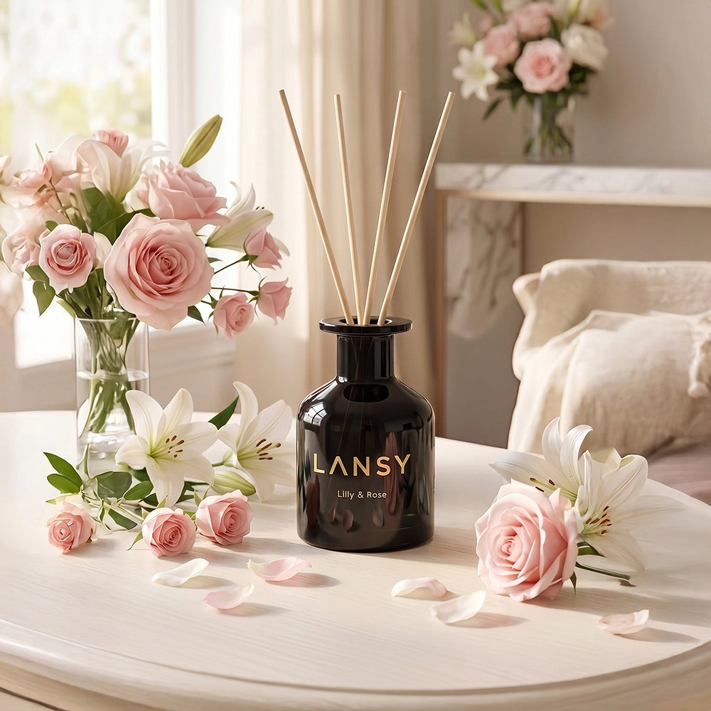 LANSY reed diffuser with pink roses, white lilies and petals on a white table.