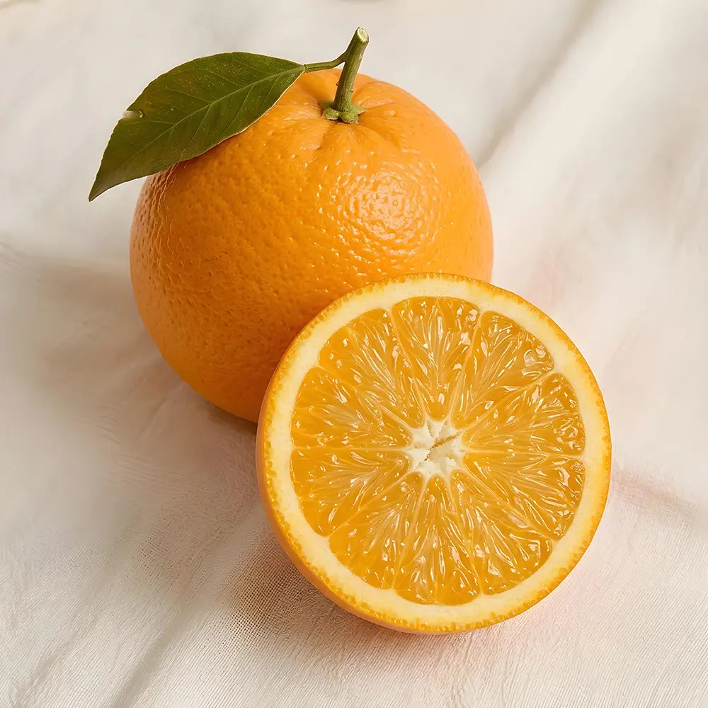 Whole and sliced orange with a green leaf on a light fabric surface.