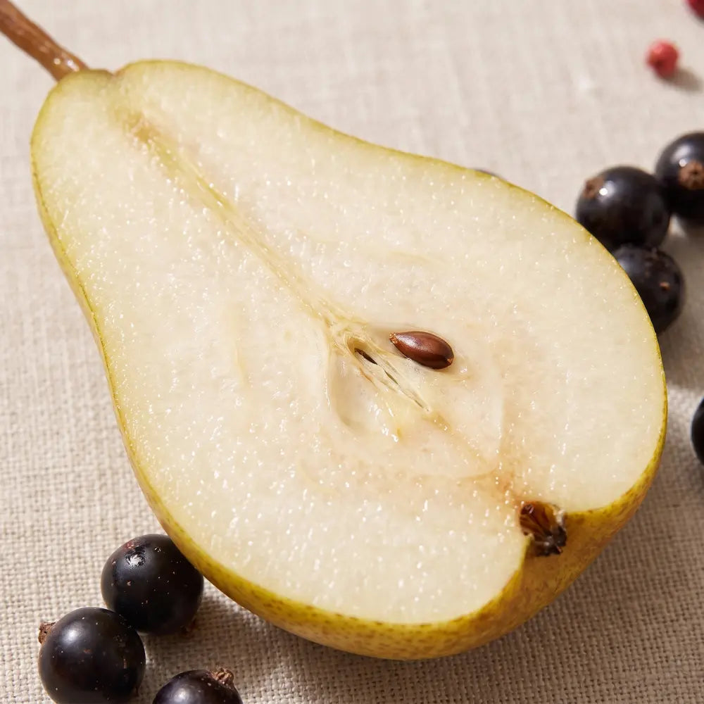 Halved yellow-green pear with dark berries on a soft beige fabric.