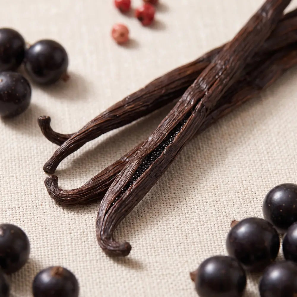 Dark vanilla beans with black and red peppercorns on textured beige fabric.