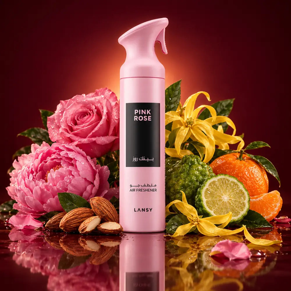 A pink spray bottle of Lansy Pink Rose Air Freshener, styled with pink roses, yellow flowers, limes, and almonds on a reflective dark red surface.